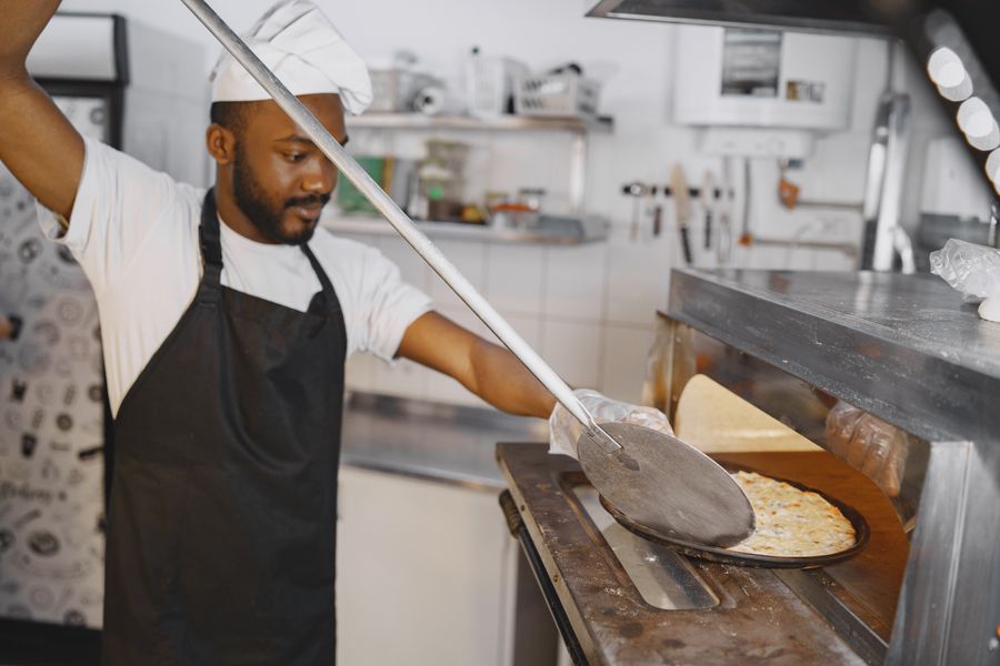 Maestro retirando una pizza del horno de leña con pala de madera